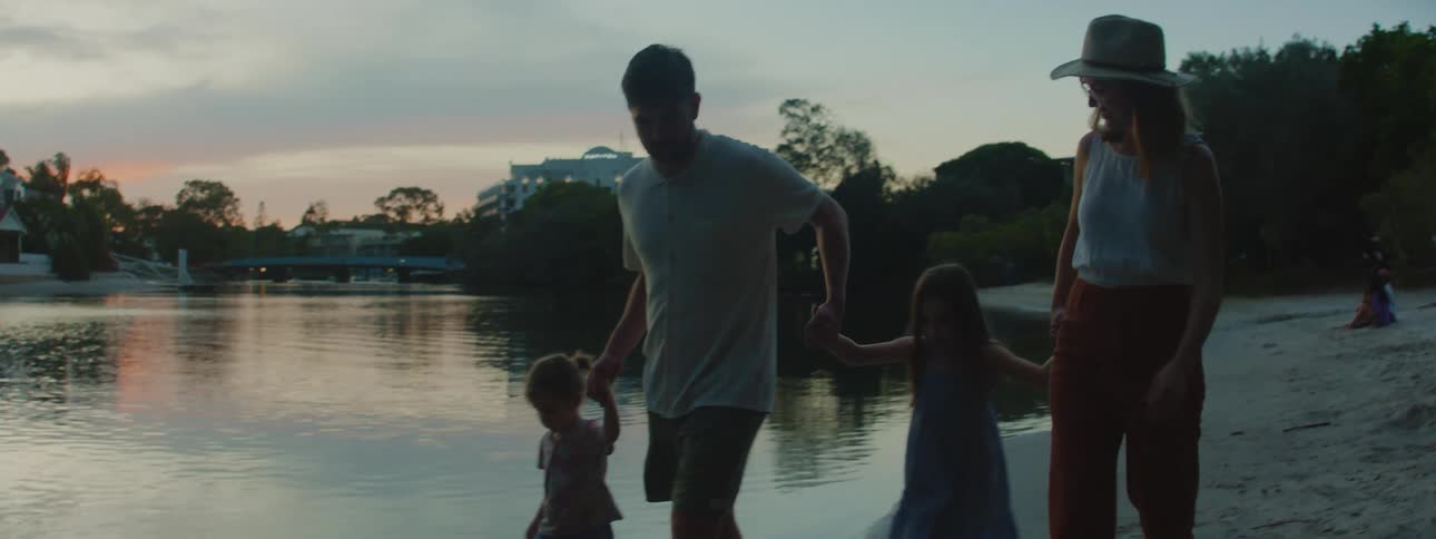 Family holding hands walk over the sand near a lake at sunset