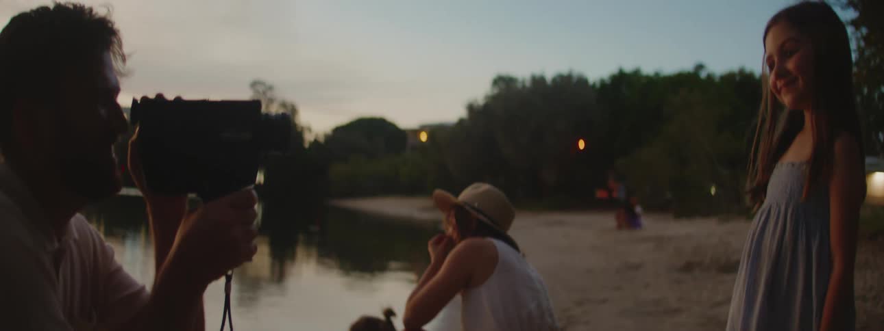 Father films daughter with blue dress on beach at sunset