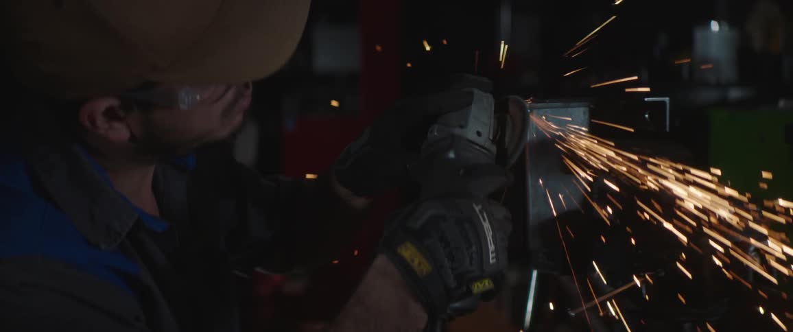 Car mechanic with brown cap goggles and gloves cuts metal with a handheld circular saw at the garage