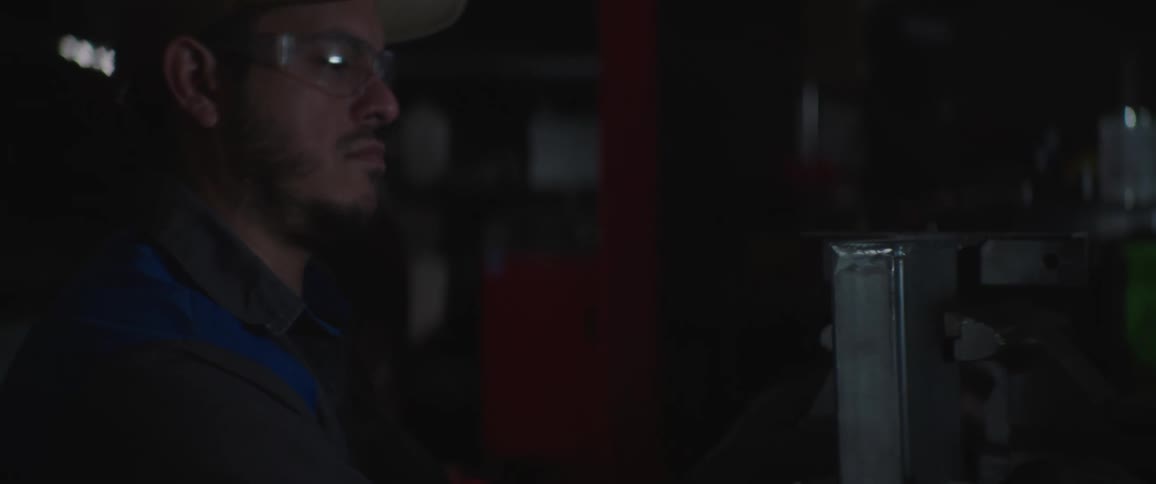 A male mechanic wearing safety glasses works in a darkened workspace