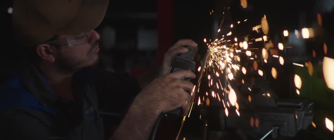 A man wears safety goggles while using a grinder on metal