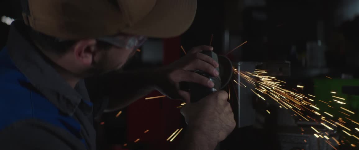 A man uses a grinder on a piece of metal while wearing protective glasses