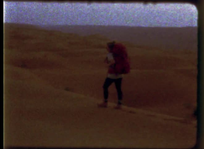 A woman wearing a backpack walks along the sand dunes