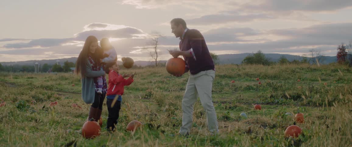 A family picks out pumpkins in a patch at sunset