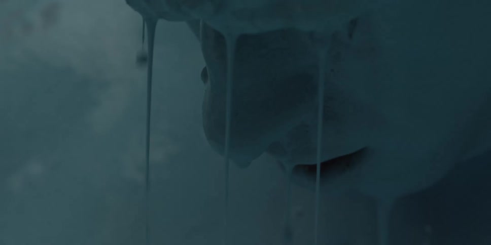 A man sits in a vat with blue liquid dripping off his head and face