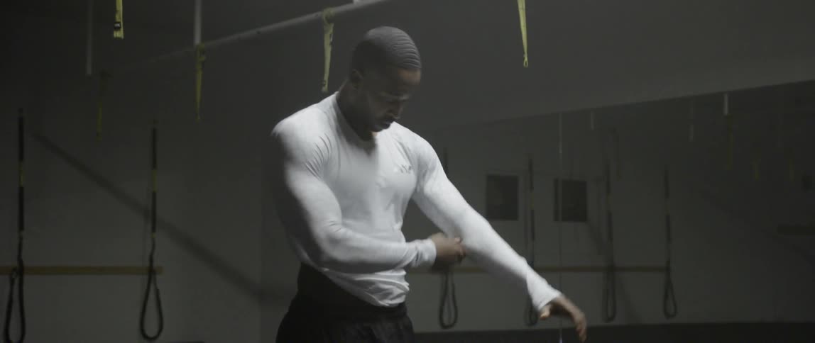 A man standing in a gym is putting on a shirt and stretching