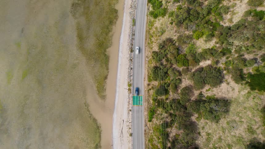 Vehicles drive down highway past scrubland and sandy terrain