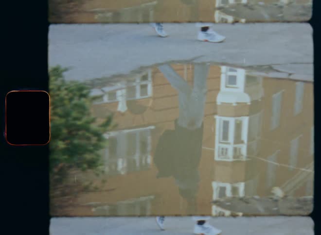 Pedestrian walks past puddle reflecting them and nearby apartment building