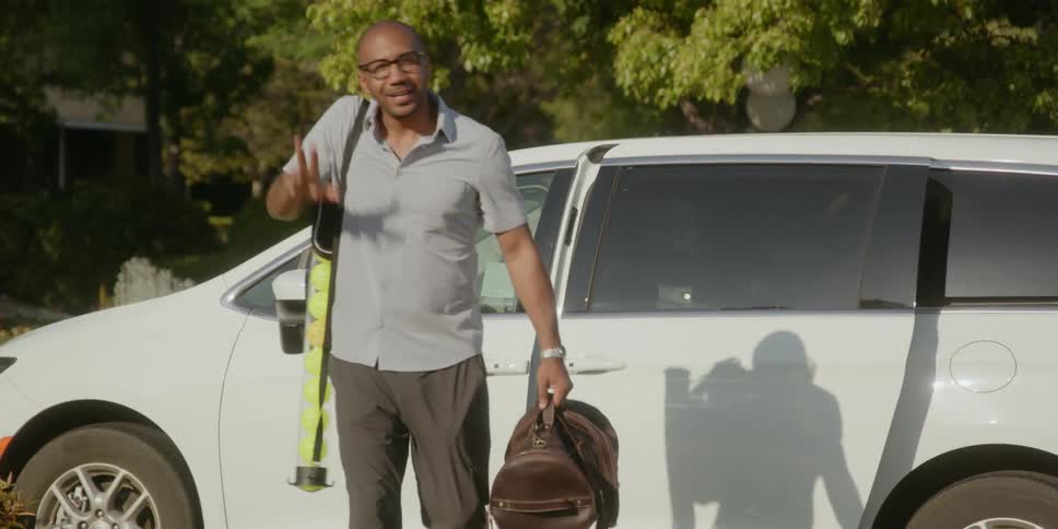 Man carrying cylinder full of balls closes car and walks forward to wave a greeting