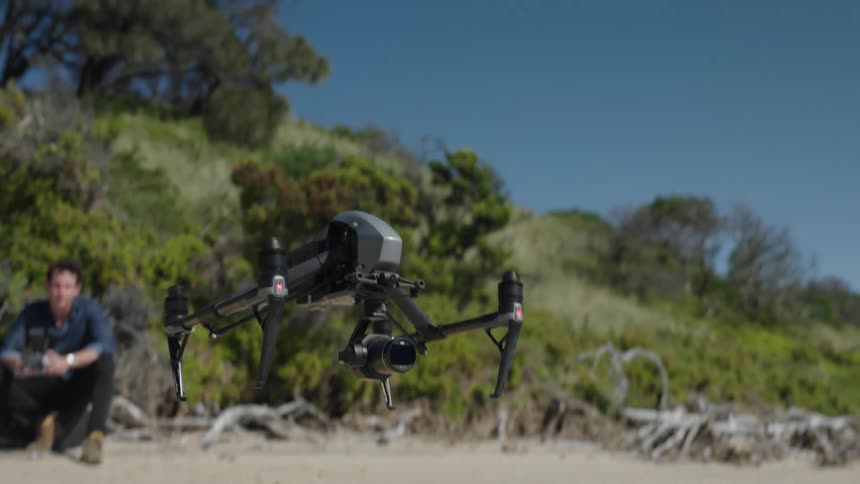 Drone operator watches drone launch from sand into blue sky