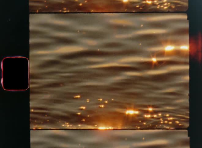 Abstract close-up of the reflection of warm golden sunlight on the surface of the water as waves roll into the gravelly shore creating flickering light and dynamic movement while the sun is setting or rising and shining
