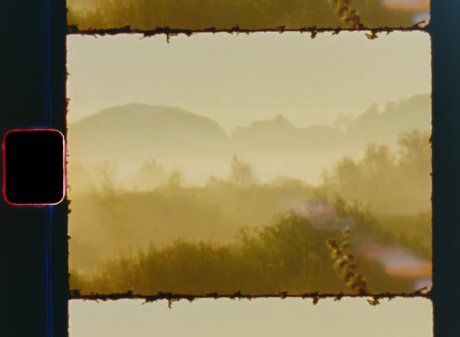 The layers of the hilly landscape are covered in fog and mist during the golden sunrise of a foggy or misty autumn morning with mountains and hills covered in trees and bushes on vintage Super 8 film