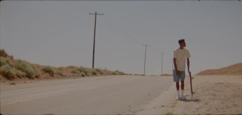 A man stands on the side of the road with his skateboard