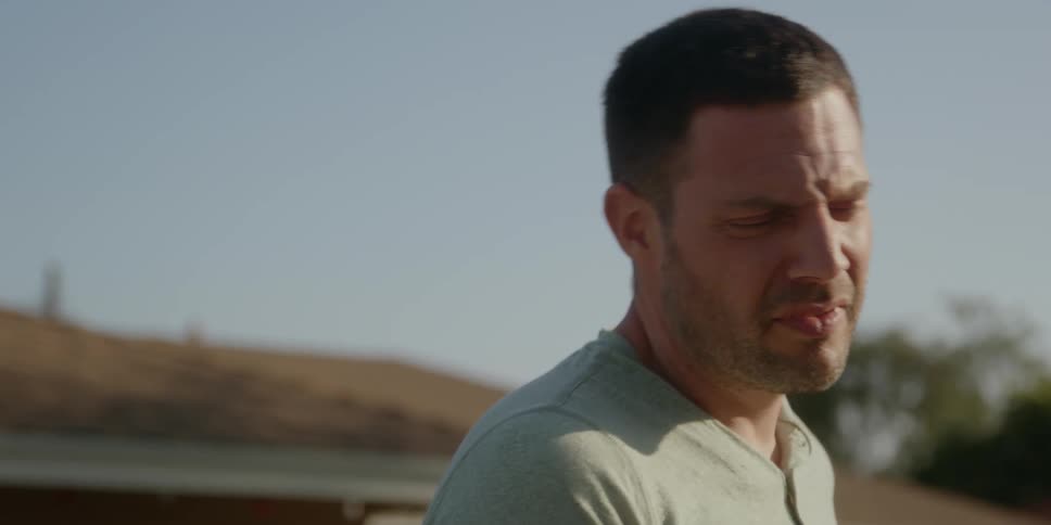 Man sighs and talks while standing with house in the background