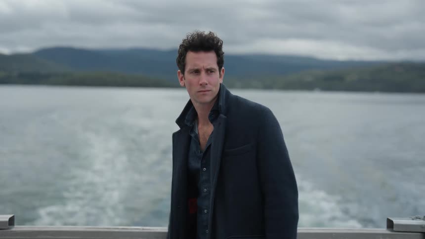 Contemplative man in an overcoat standing on the motorized boat at the lake admiring the scenery