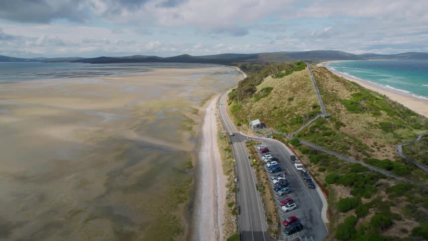 An aerial shot of a road on a narrow strip of land next to a beach