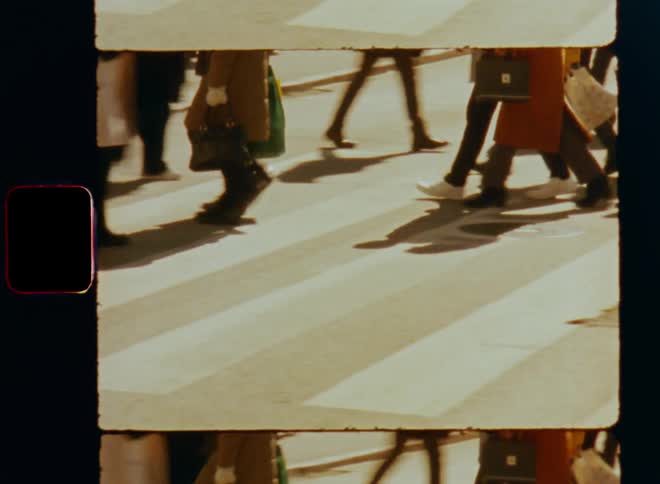 A crowd of pedestrians walk along a crosswalk during the day