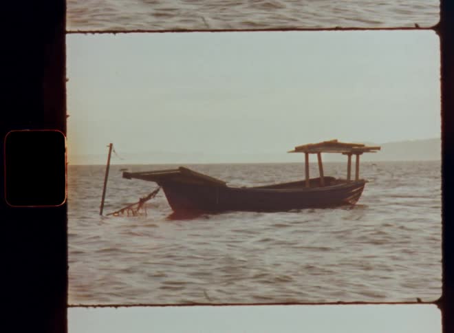 Vintage footage of a small wooden fishing boat tied to a pole floating in the sea and moving as the wind causes ripples and waves on a sunny day by the Baltic Coast