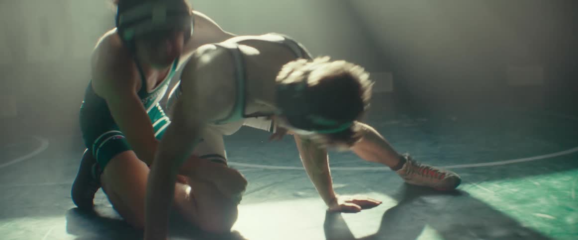 A pair of young wrestlers wrestle in a dimly lit gym during the day