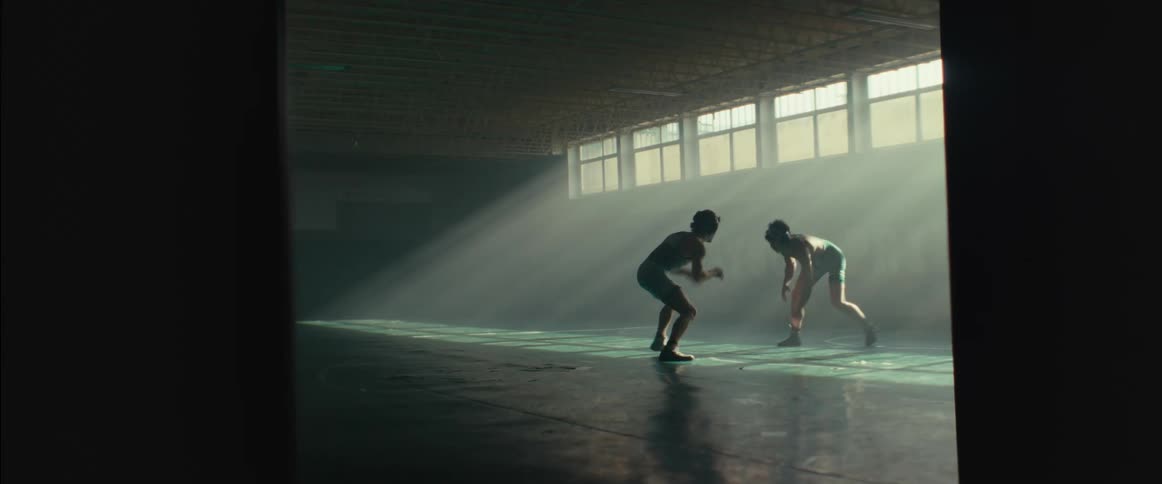Two young men wearing wrestling clothes practicing wrestling in the middle of an empty gym during the day