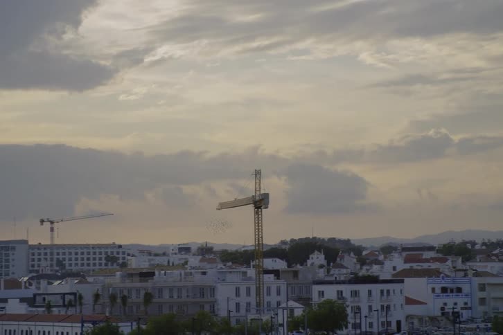 Construction cranes tower over apartment buildings with mountains on the horizon