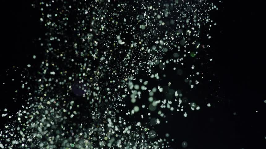 White particles float downward through black background with scattered light spots