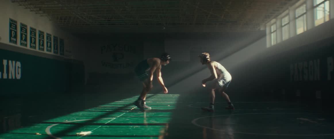 A pair of wrestlers shake hands before beginning to wrestle in a dimly lit gym during the day
