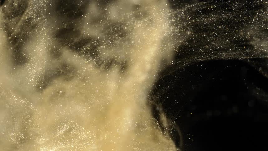 Golden sparkling dust particles flow across dark background