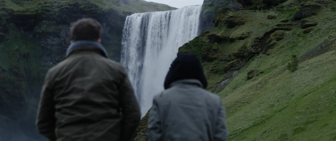 Two people hike near a large waterfall