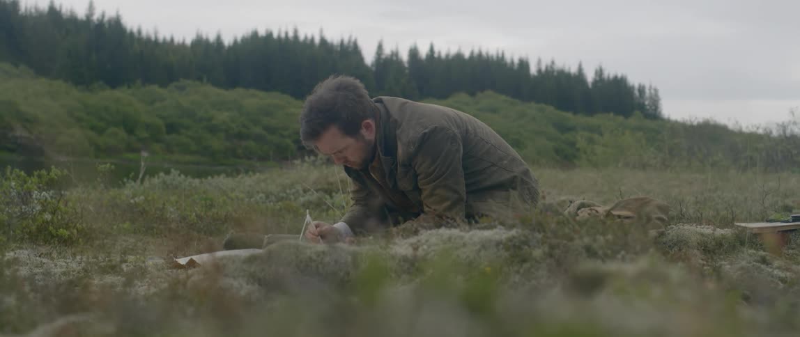 A man crouches in a field to write something down