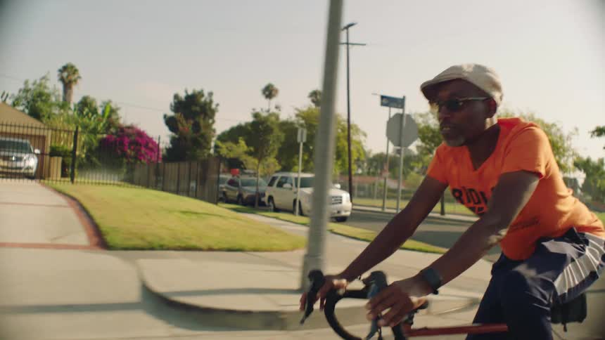 A man rides a bicycle along a street through a residential area during the day