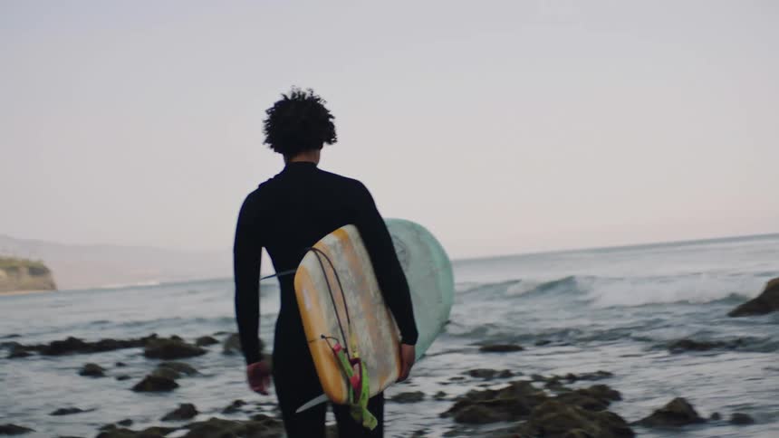 A woman is carrying his surfboard to the water