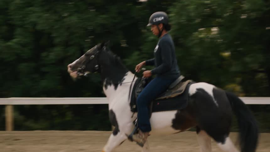 A woman rides a horse around an enclosure during the day