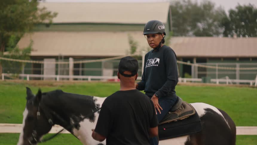 A man gestures while talking to a woman sitting on a horse outdoors during the day