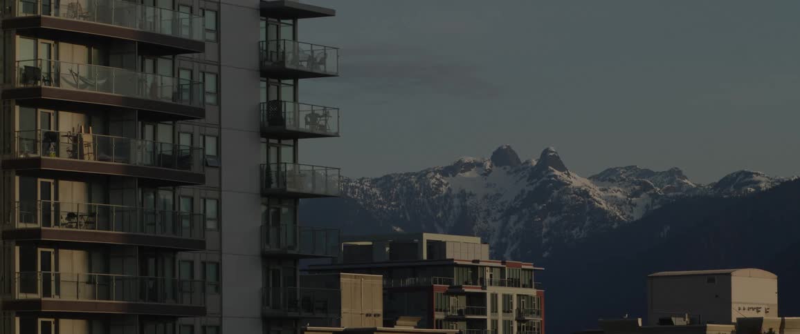 Apartment building towers over snow covered mountains and shorter buildings