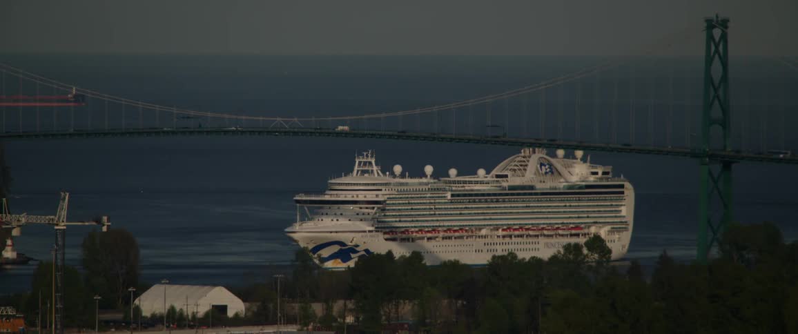 A large cruise ship sails under a suspension bridge