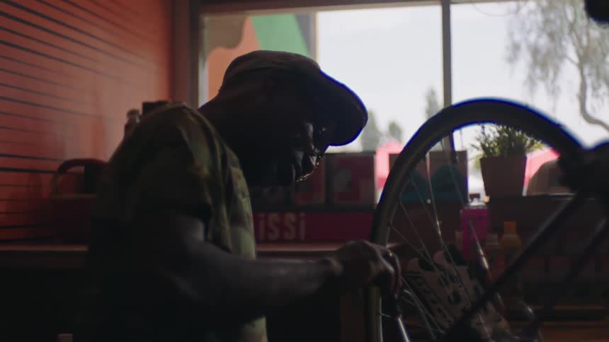 Man repairing a bicycle wheel using a tool in his workshop