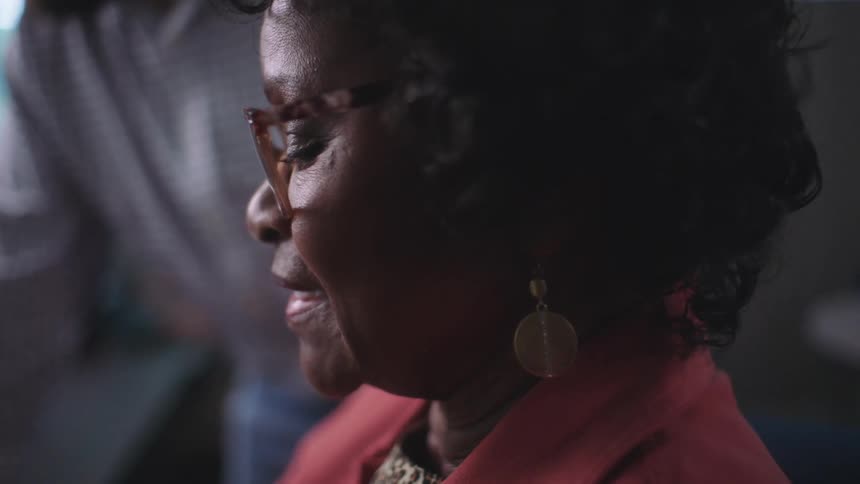Elderly black woman sitting down talking next to a man standing up