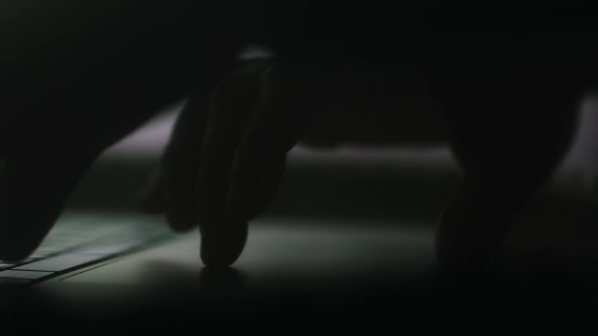 A person uses the touch pad on a laptop in a dimly lit room