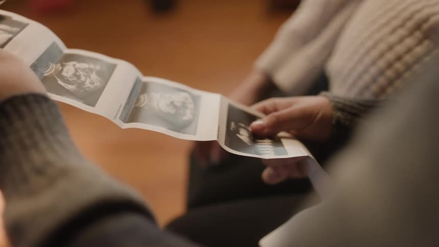 Expectant mother sits with man looking at ultrasound pictures