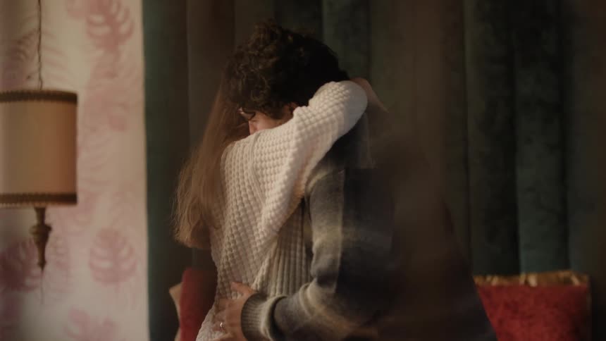 Couple slow dances in room with pink patterned wallpaper