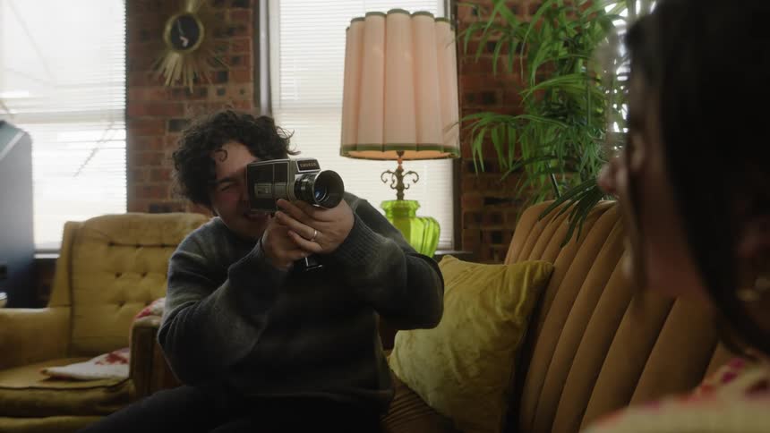 Man sitting on sofa filming a woman with an oldfashioned camera