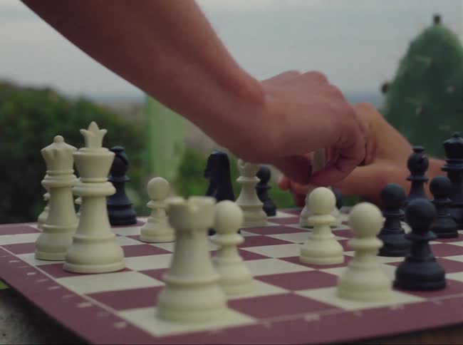 Two men playing chess outside while smoking and drinking