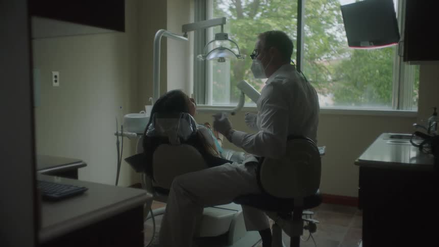 Dentist talks to patient lying in dental chair and examines their mouth