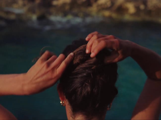 A woman tying back her hair before jumping into the sea from a cliff