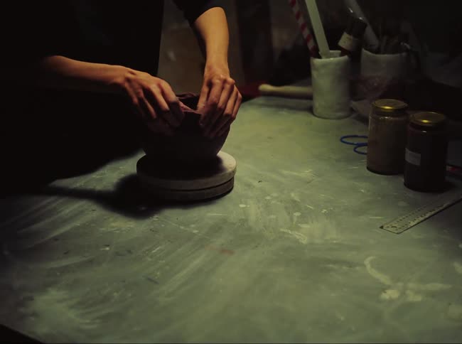 Potter shapes clay pot on workshop turn table