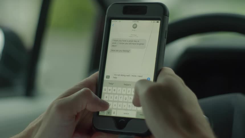 A person sitting in a car picks up their smartphone and begins to write a text message