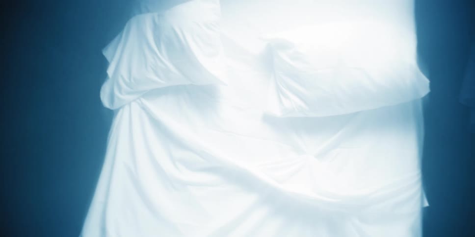A close up of a bed with white sheets and pillow standing upright and moving forward and back