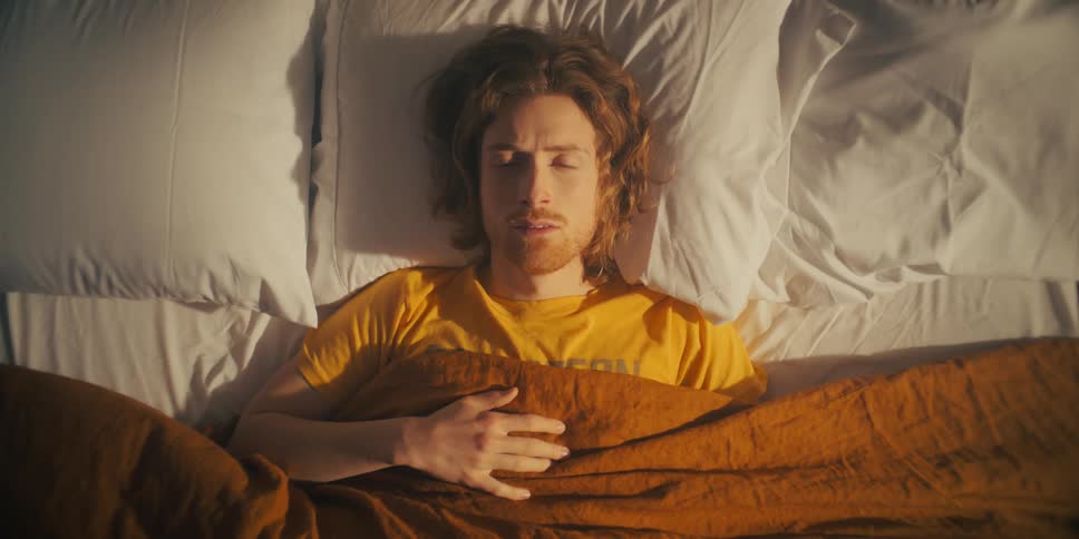 A man lying in bed closes his eyes and turns his head