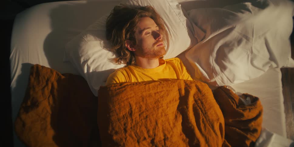 A man sleeping in bed rolls over and then opens his eyes